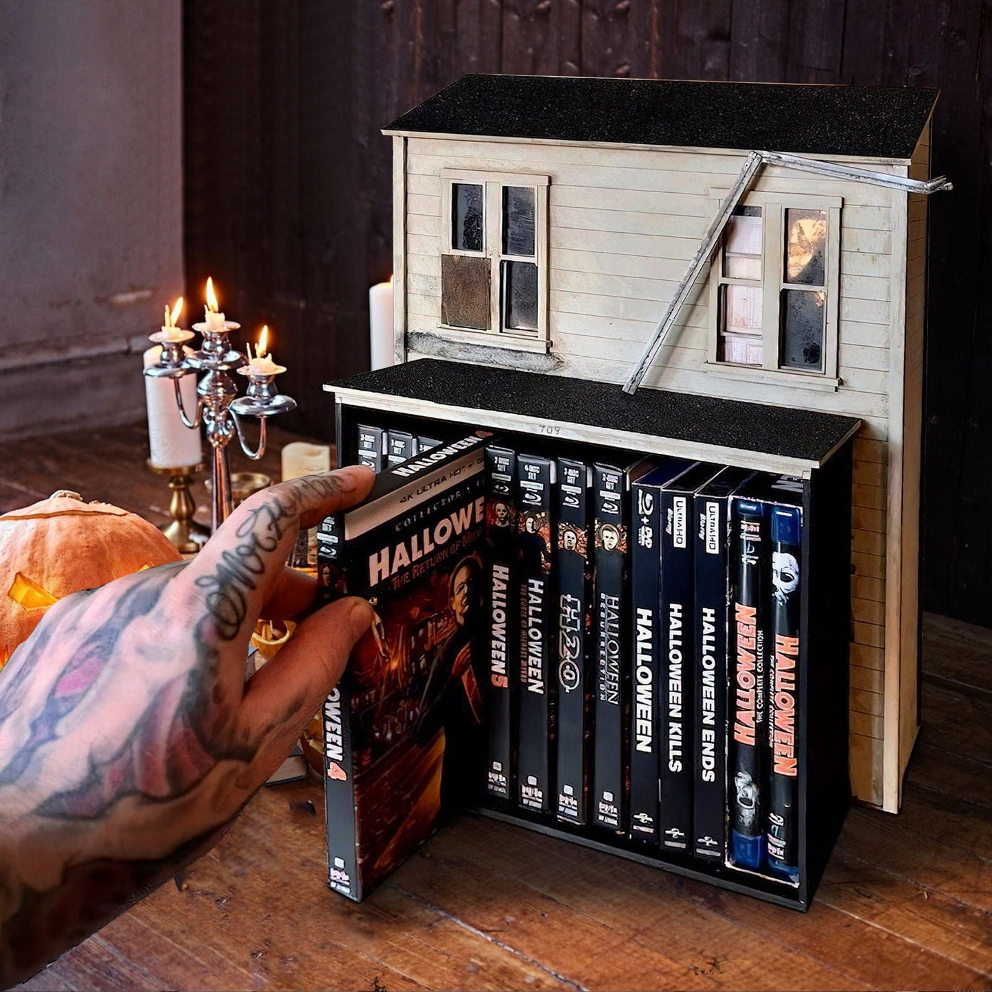 Collection of 'Halloween' movie DVDs inside a miniature house model with a tattooed hand reaching in.