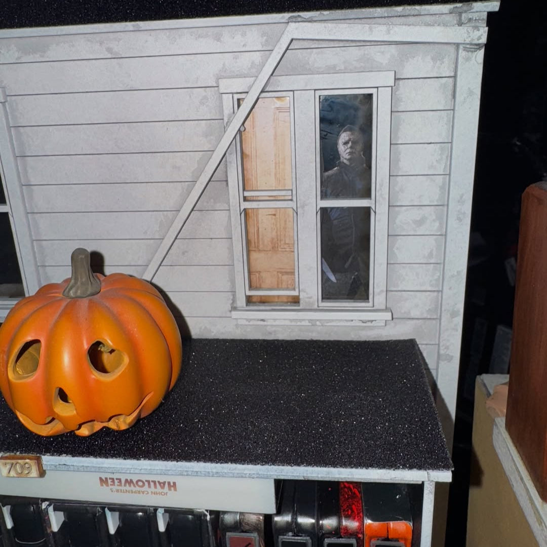 Small model of a house with a pumpkin on a shelf against a dark background