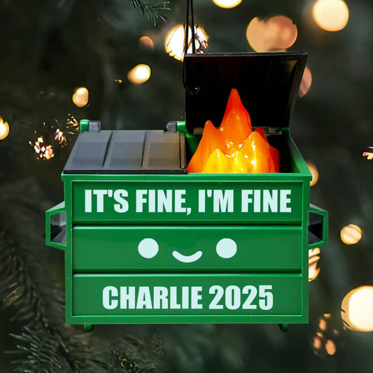 Green dumpster ornament with 'It's Fine, I'm Fine' text and 'Charlie 2025' on a blurred Christmas tree background.